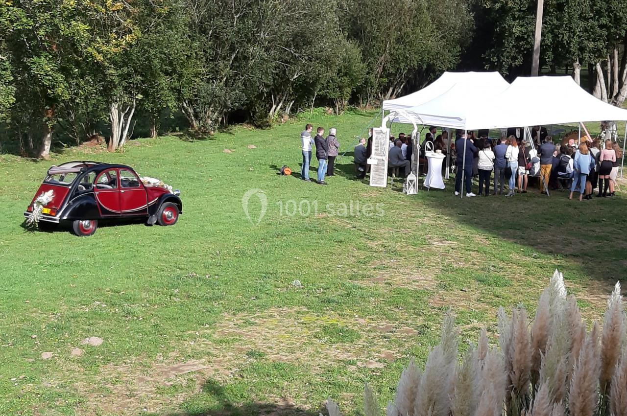 Une voiture ancienne rouge garée sur une pelouse près d'une tente blanche abritant un groupe de personnes.