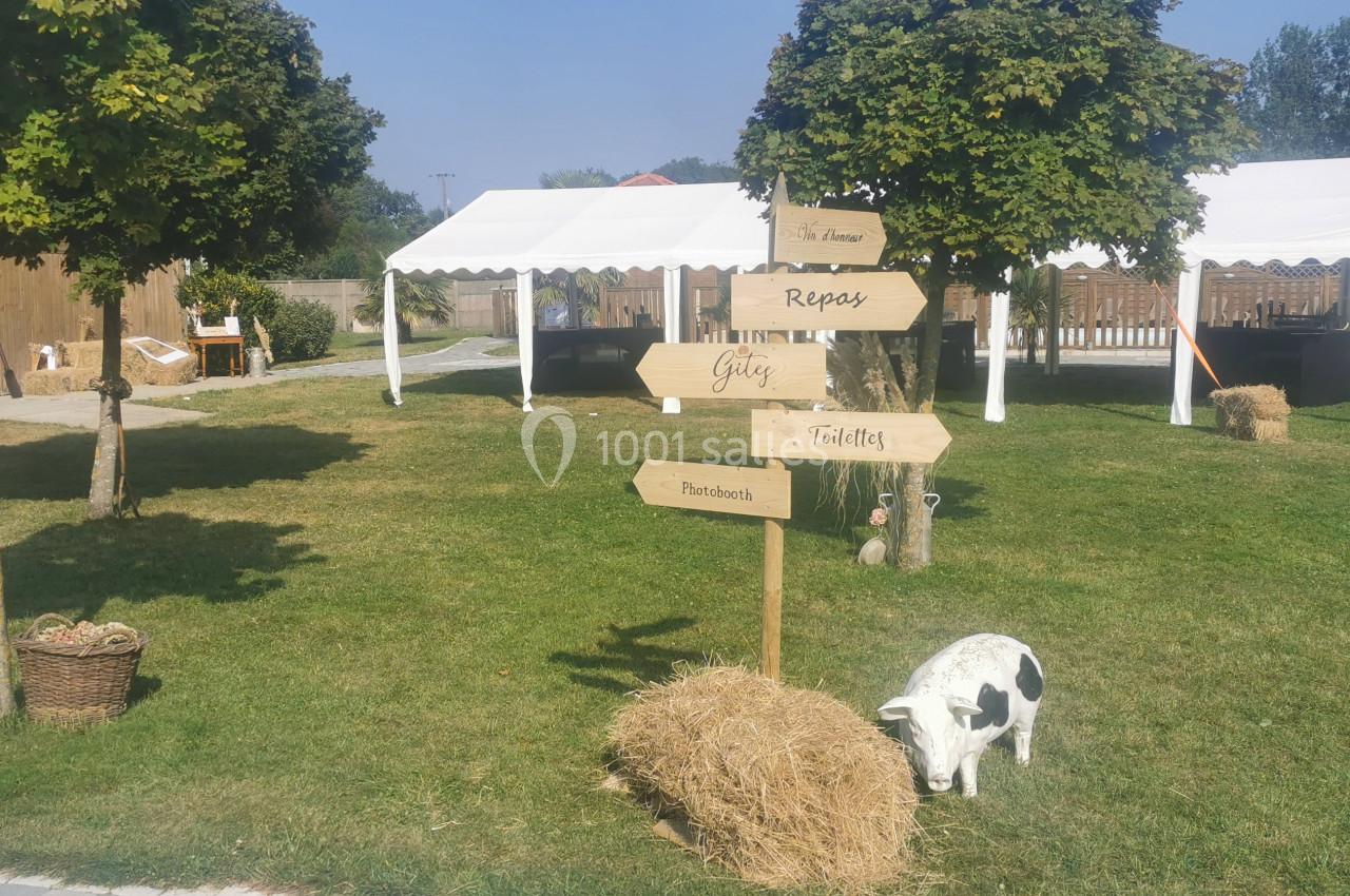 Panneaux en bois indiquant différentes directions dans un espace extérieur avec tentes blanches, arbres et une décoration…