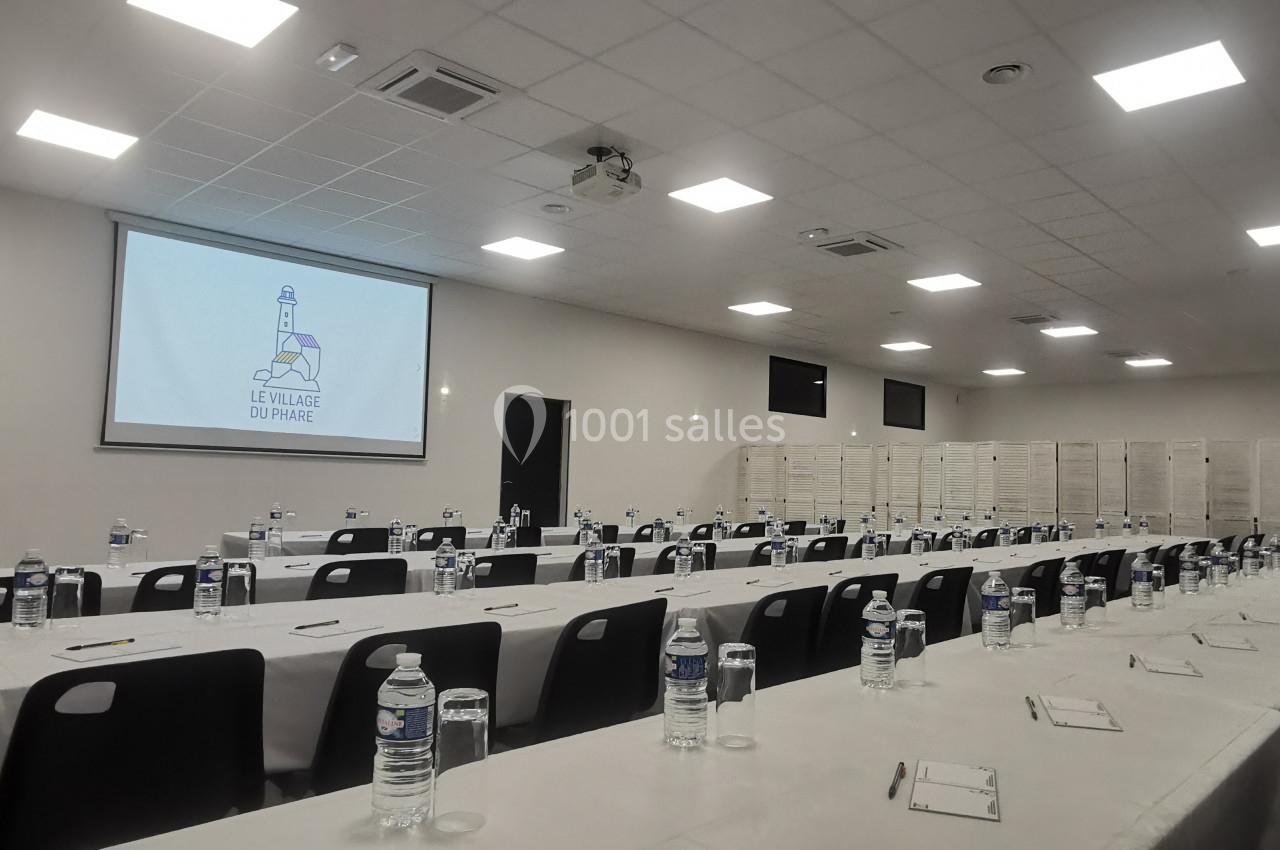 Salle de conférence avec des tables alignées, bouteilles d'eau, carnets, et un écran affichant un logo.