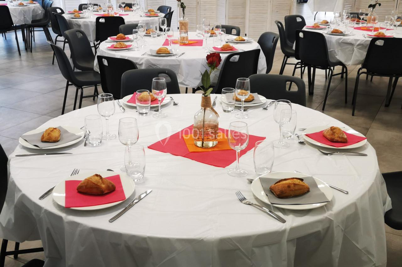 Salle de réception avec tables rondes dressées, nappes blanches, serviettes colorées et vaisselle prête pour un repas.