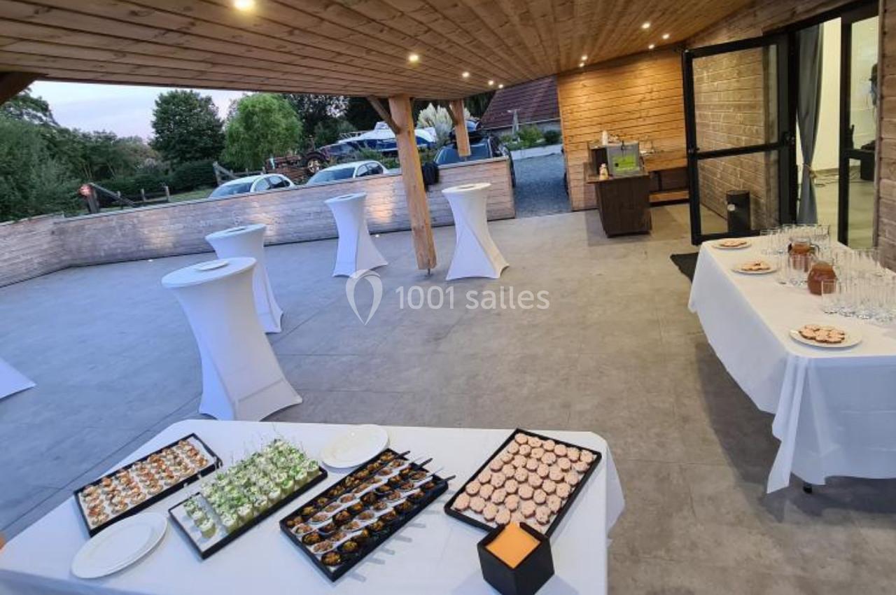 Terrasse aménagée pour un événement avec tables hautes, buffet de canapés et vue sur un espace extérieur verdoyant.