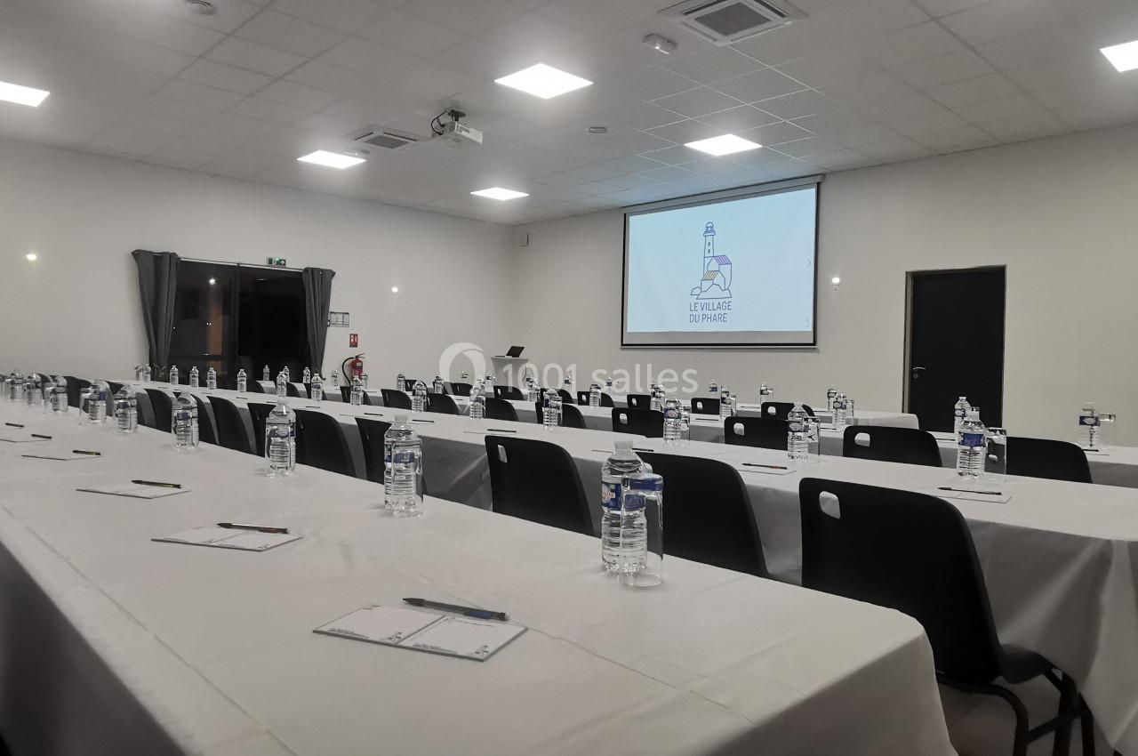 Salle de conférence aménagée avec des tables alignées, des bouteilles d'eau, des blocs-notes et un écran de projection…