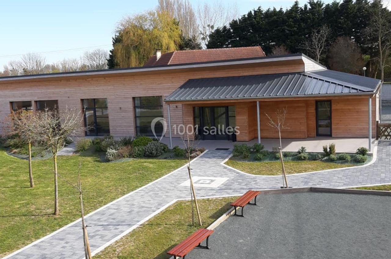Bâtiment moderne en bois avec toit en métal, entouré d'un espace vert aménagé et de bancs sur une allée pavée.