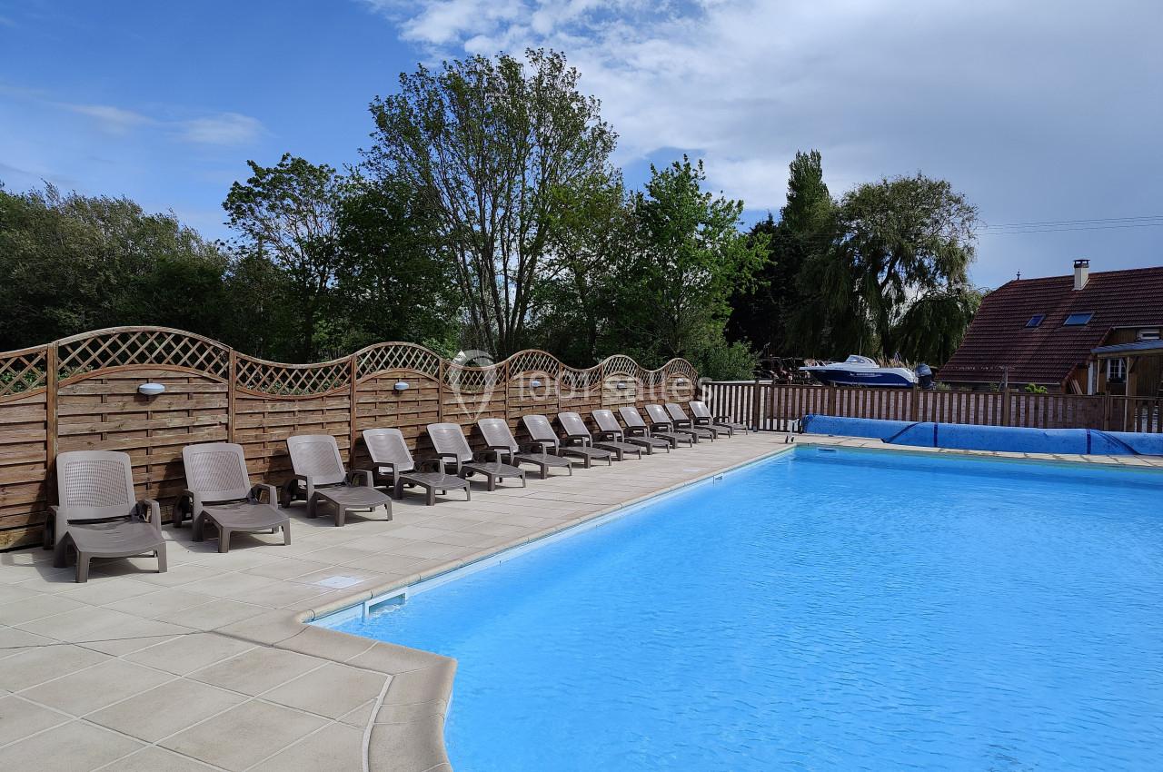 Piscine extérieure avec chaises longues alignées sur une terrasse, entourée de clôtures en bois et de végétation.
