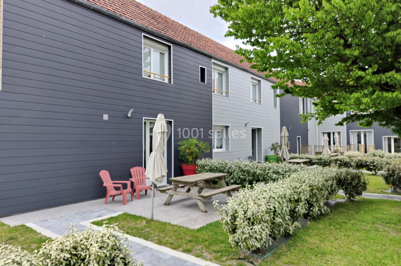 Façade de maisons modernes avec terrasse aménagée, mobilier de jardin et végétation environnante.