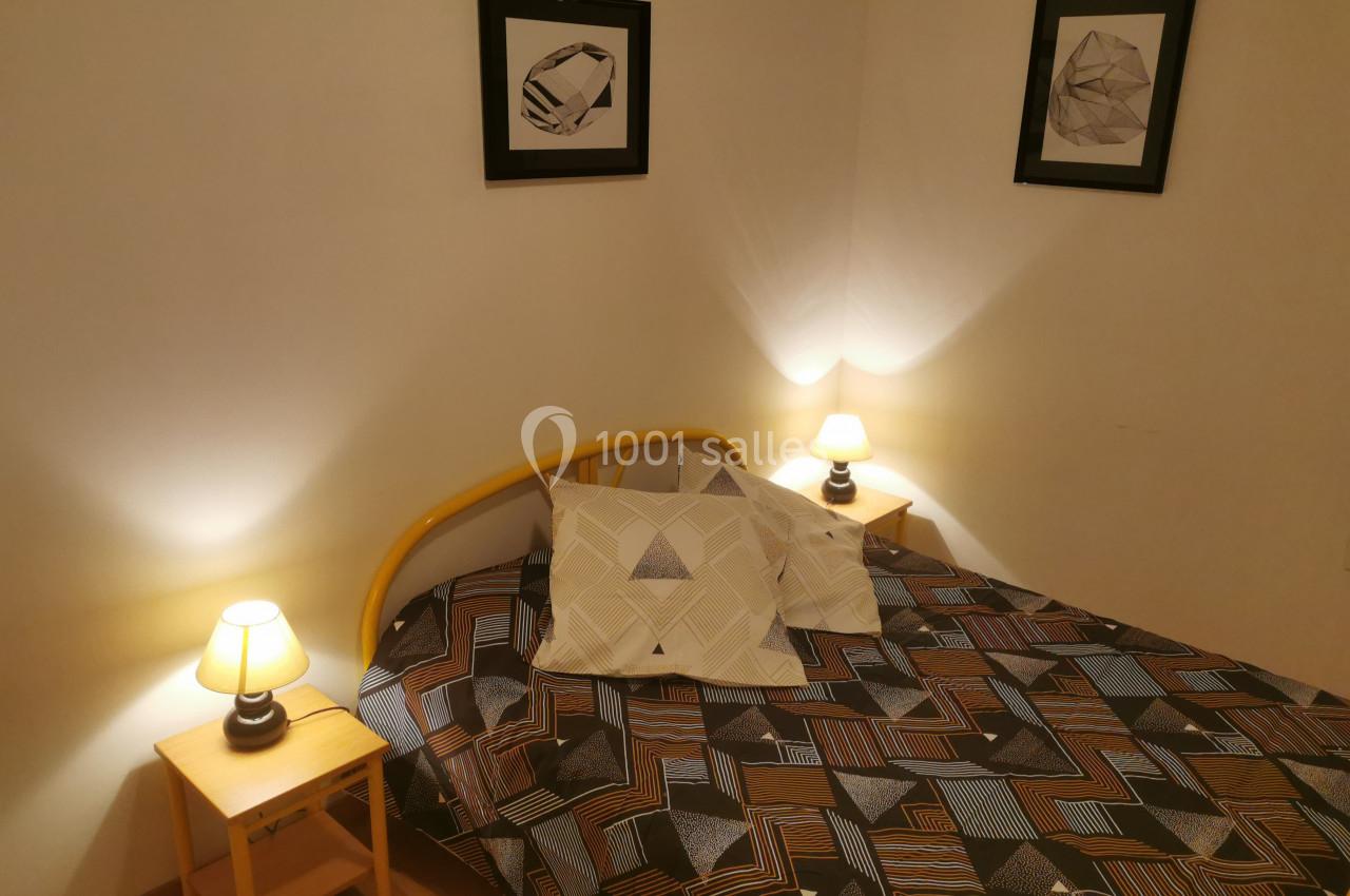 Lit double avec housse géométrique, encadré par deux tables de chevet avec lampes allumées, dans une chambre sobre.