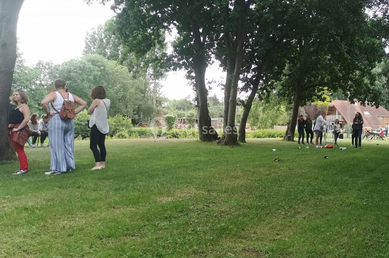 Personnes discutant ou jouant sur une pelouse entourée d'arbres, avec des bâtiments en arrière-plan.