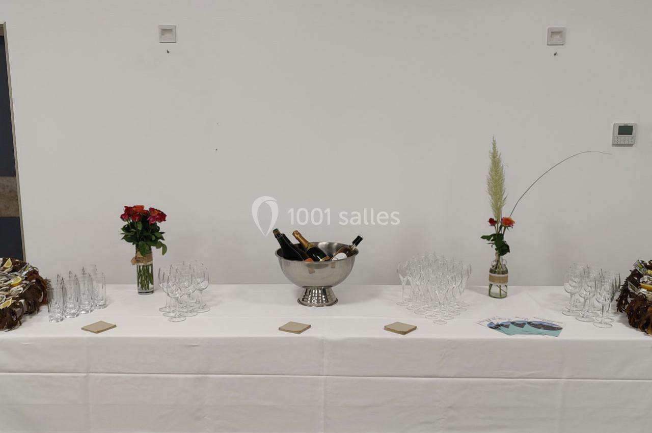 Table dressée avec des verres, un seau à champagne contenant des bouteilles, des fleurs et des brochures.