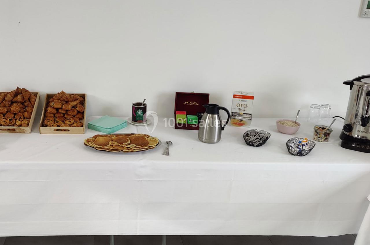 Table dressée avec viennoiseries, pancakes, thé, café, bols de céréales, verres et une bouilloire.