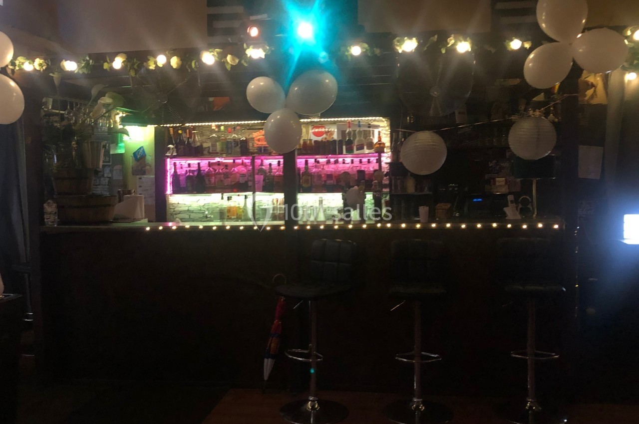 Bar décoré avec des guirlandes lumineuses, des ballons blancs et un éclairage coloré au-dessus du comptoir.