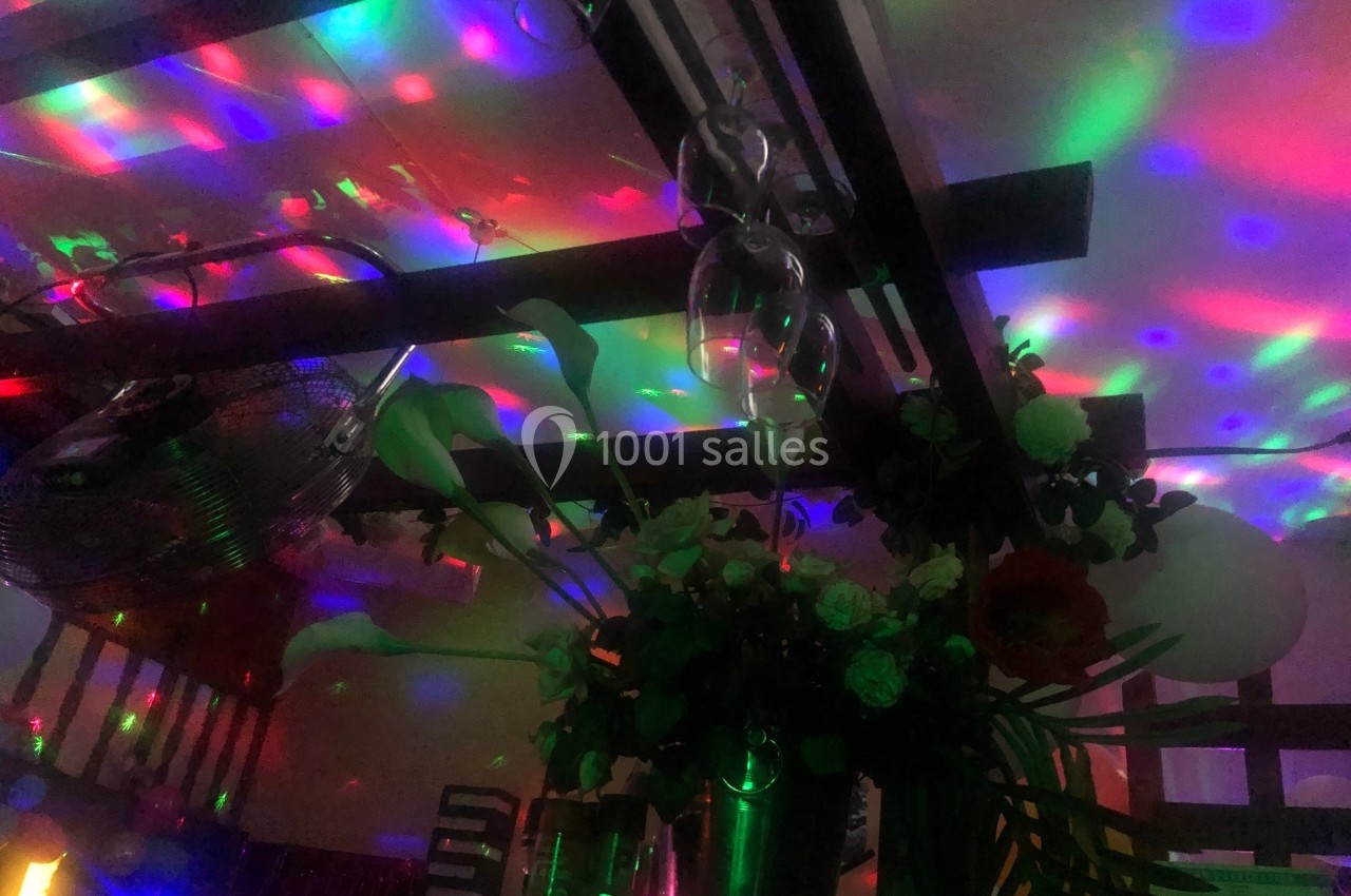 Lumières colorées projetées au plafond avec des verres suspendus et un bouquet de fleurs en premier plan.