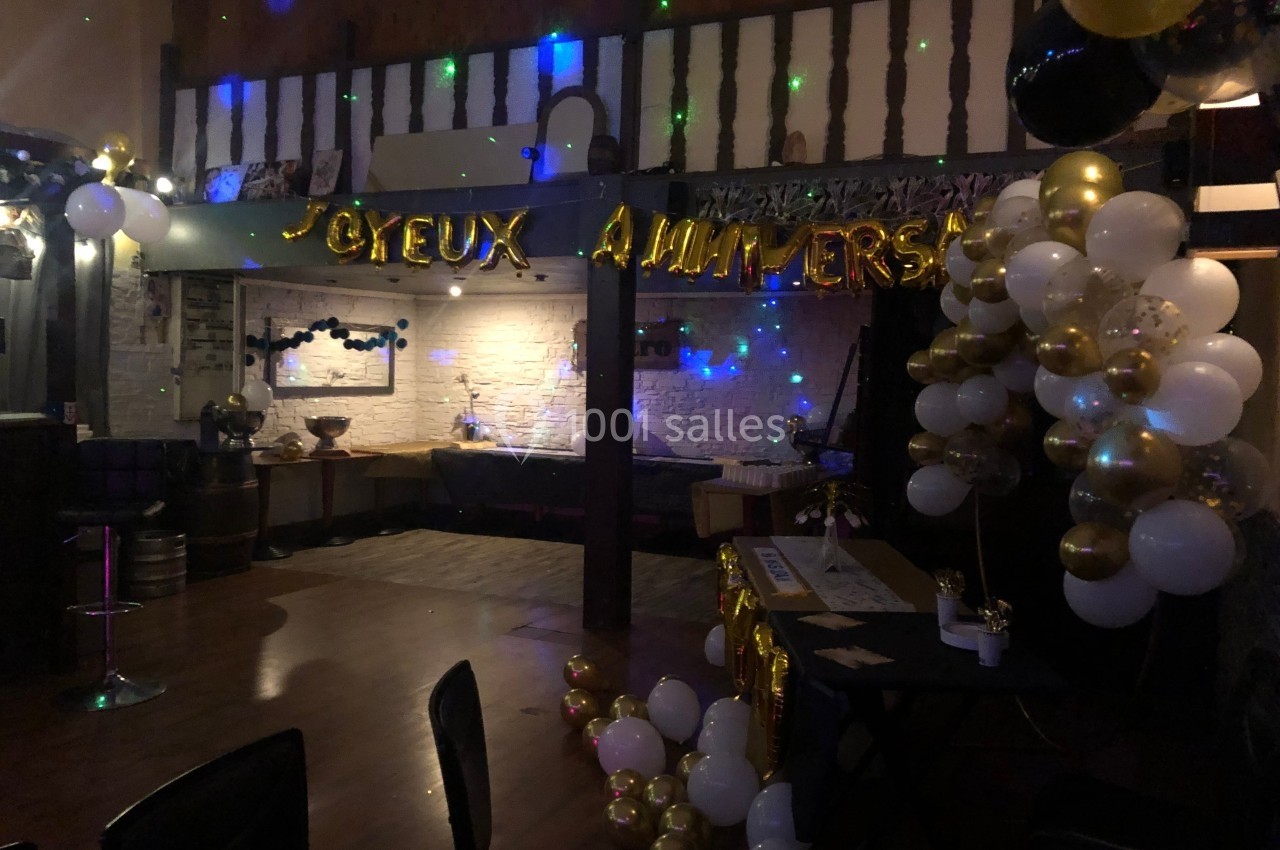 Décoration d'anniversaire avec ballons blancs, dorés et noirs, guirlande ’Joyeux Anniversaire’ et lumières colorées.