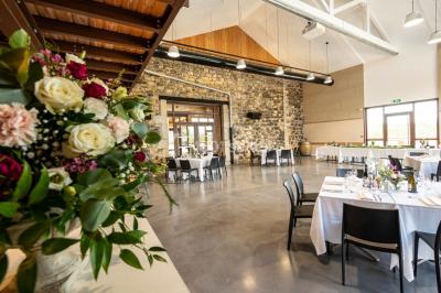 Tables dressées avec nappes blanches et chaises en bois sous des voiles d'ombrage dans une cour extérieure ensoleillée.
