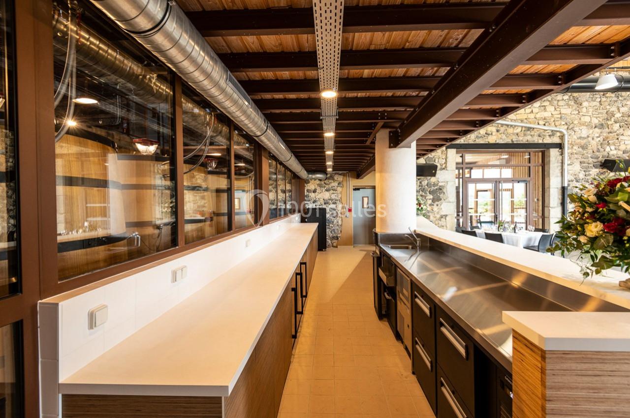 Cuisine professionnelle moderne avec plans de travail en inox et bois, éclairage naturel et murs en pierre apparente.