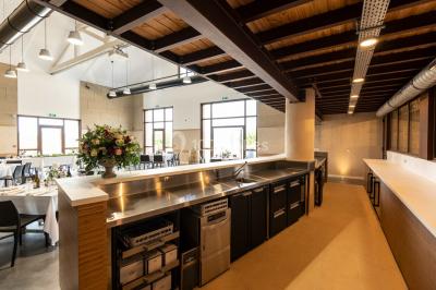 Tables dressées avec nappes blanches et chaises en bois sous des voiles d'ombrage dans une cour extérieure ensoleillée.