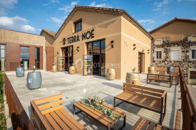 Tables dressées avec nappes blanches et chaises en bois sous des voiles d'ombrage dans une cour extérieure ensoleillée.
