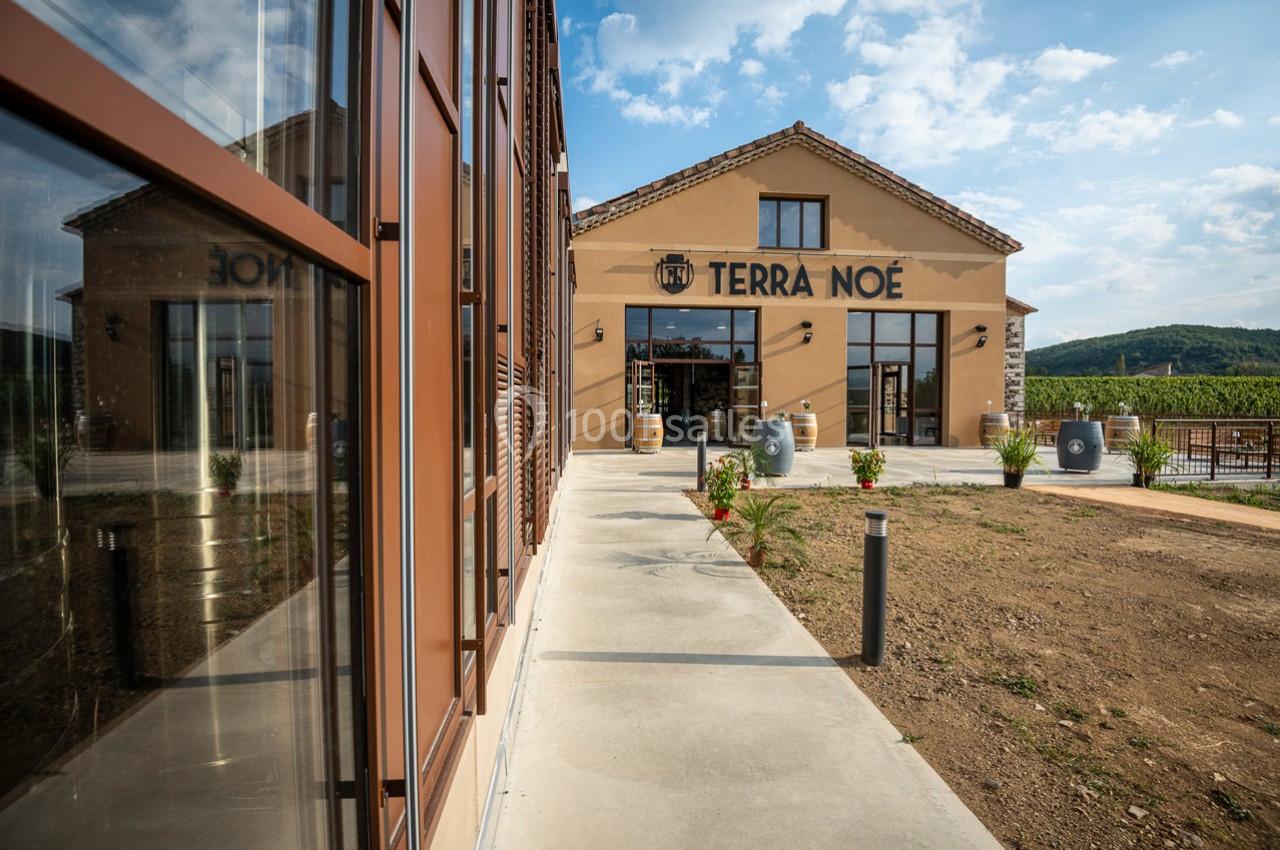 Façade d'un bâtiment en pierre avec enseigne ’Terra Noé’, entouré de vignes et d'un ciel partiellement nuageux.