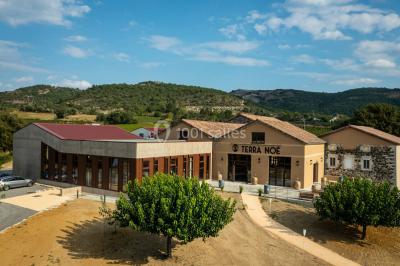 Tables dressées avec nappes blanches et chaises en bois sous des voiles d'ombrage dans une cour extérieure ensoleillée.
