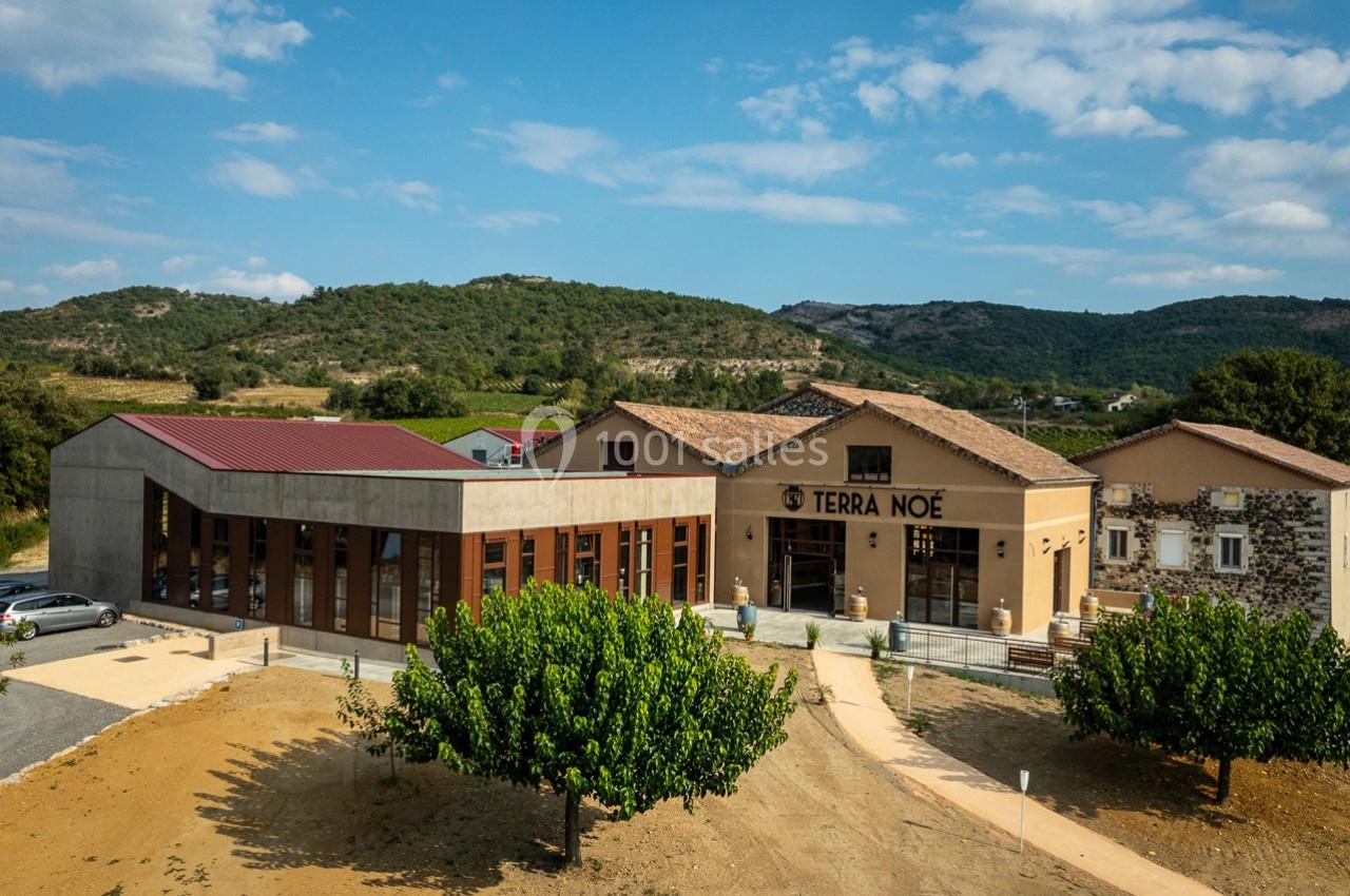 Vue aérienne d'un bâtiment moderne et traditionnel entouré de végétation et de collines sous un ciel dégagé.