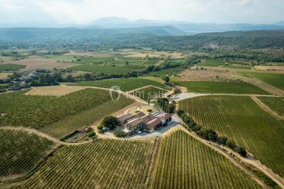 Tables dressées avec nappes blanches et chaises en bois sous des voiles d'ombrage dans une cour extérieure ensoleillée.