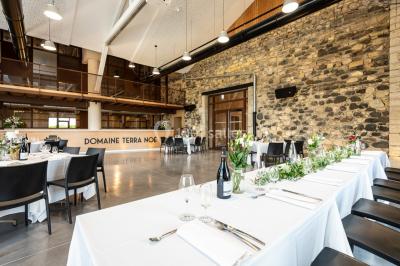 Tables dressées avec nappes blanches et chaises en bois sous des voiles d'ombrage dans une cour extérieure ensoleillée.