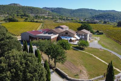 Tables dressées avec nappes blanches et chaises en bois sous des voiles d'ombrage dans une cour extérieure ensoleillée.