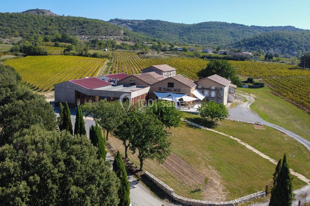 Vue aérienne d'un domaine viticole entouré de vignes et de collines verdoyantes, avec bâtiments au centre.