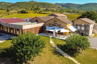 Tables dressées avec nappes blanches et chaises en bois sous des voiles d'ombrage dans une cour extérieure ensoleillée.