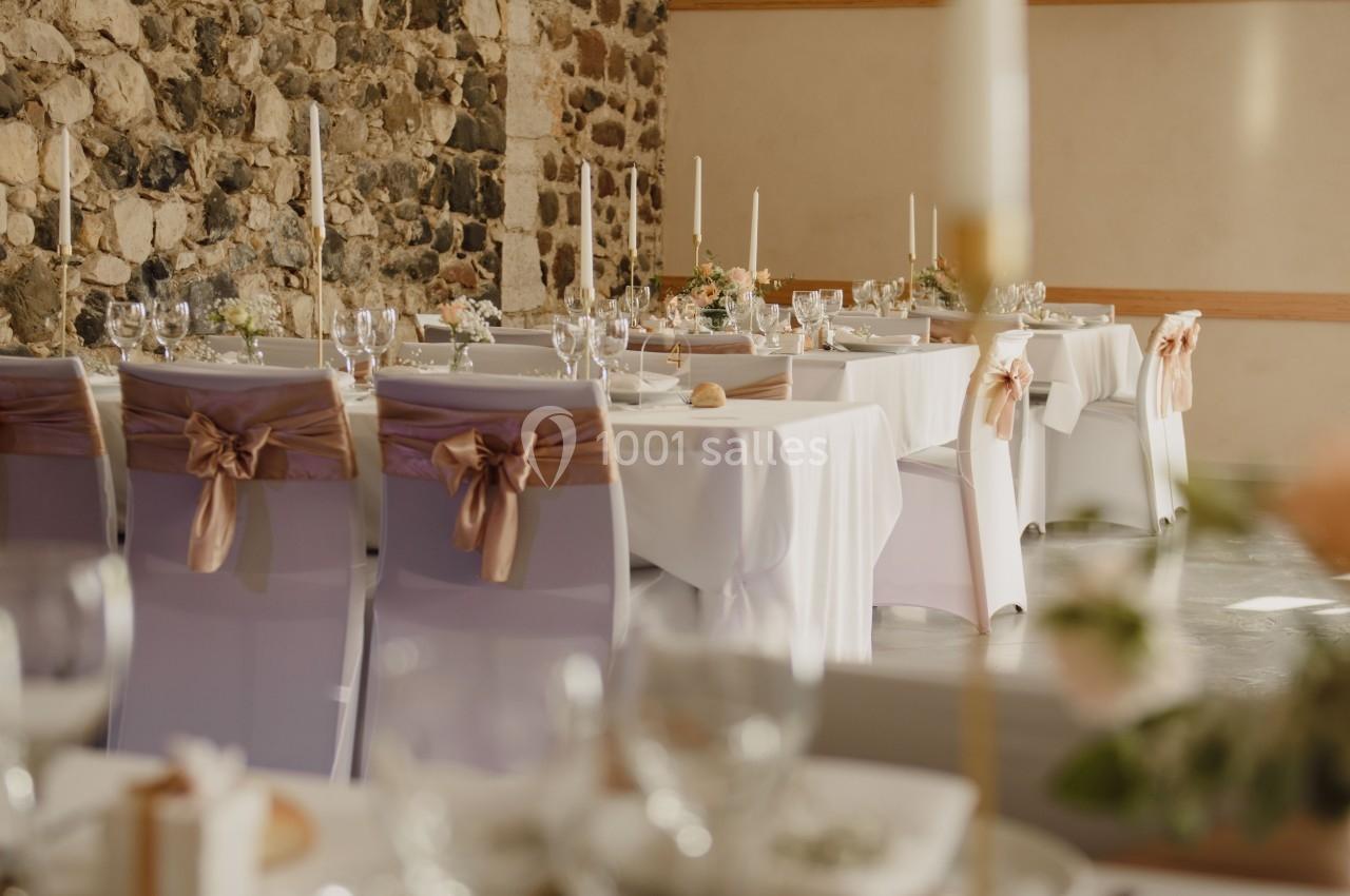 Salle de réception décorée pour un mariage avec des chaises ornées de rubans et des tables dressées avec des bougies.