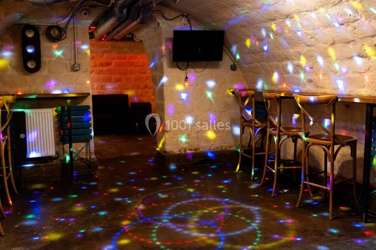 Salle voûtée avec des tables, chaises en bois et éclairage coloré projeté sur les murs et le sol.