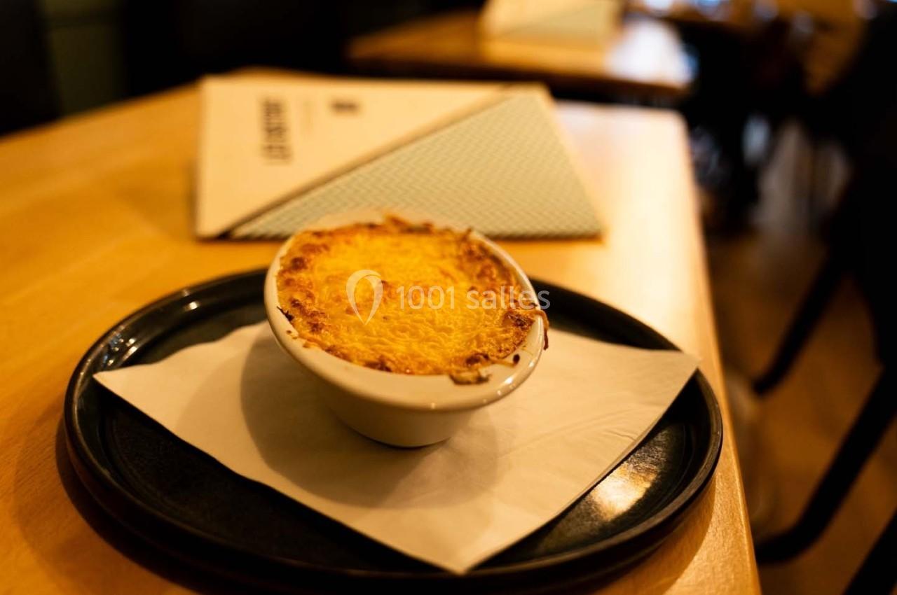 Gratin doré servi dans un petit plat blanc sur une assiette noire avec une serviette, posé sur une table en bois.