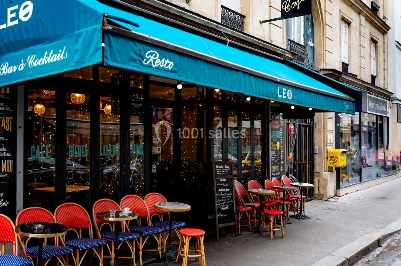 Façade d'un café-restaurant avec terrasse colorée et tables en extérieur, situé dans une rue urbaine animée.