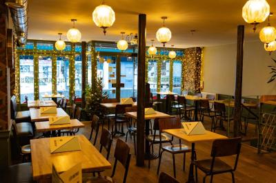 Façade d'un café-restaurant avec terrasse, chaises rouges et tables rondes, éclairage chaleureux à l'intérieur.