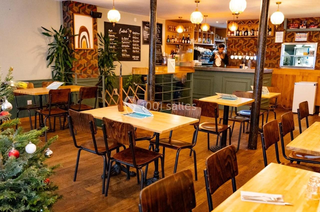 Salle de restaurant chaleureuse avec tables en bois, décorations murales colorées et un sapin de Noël décoré.