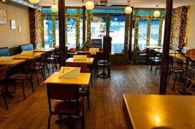 Façade d'un café-restaurant avec terrasse, chaises rouges et tables rondes, éclairage chaleureux à l'intérieur.