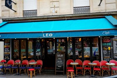 Façade d'un café-restaurant avec terrasse, chaises rouges et tables rondes, éclairage chaleureux à l'intérieur.