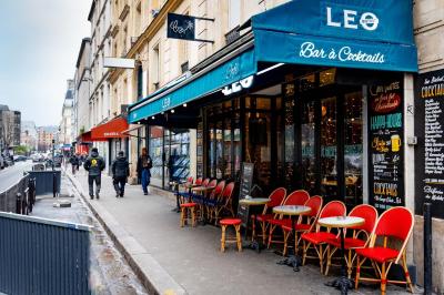 Façade d'un café-restaurant avec terrasse, chaises rouges et tables rondes, éclairage chaleureux à l'intérieur.