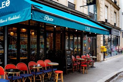 Façade d'un café-restaurant avec terrasse, chaises rouges et tables rondes, éclairage chaleureux à l'intérieur.