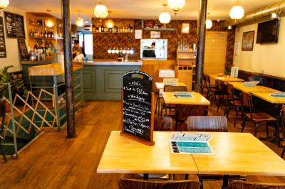 Façade d'un café-restaurant avec terrasse, chaises rouges et tables rondes, éclairage chaleureux à l'intérieur.