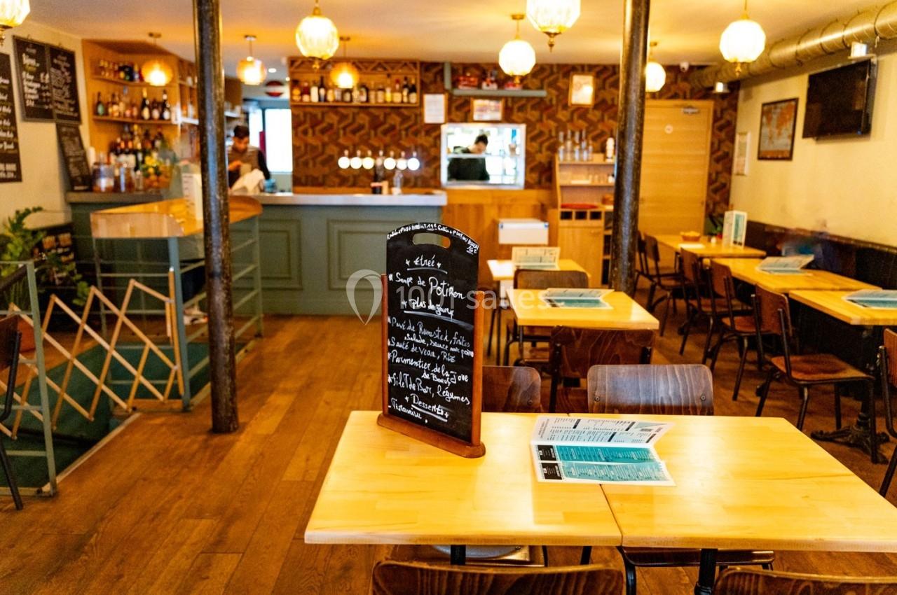 Intérieur d'un restaurant avec des tables en bois, un tableau noir affichant le menu et un bar en arrière-plan.
