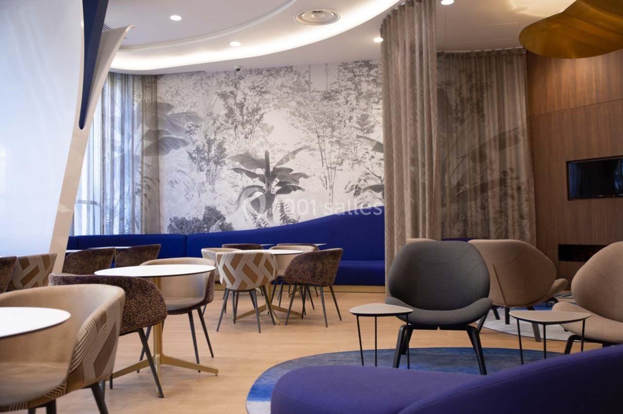 Espace lounge moderne avec fauteuils design, tables rondes et décor mural végétal en noir et blanc.