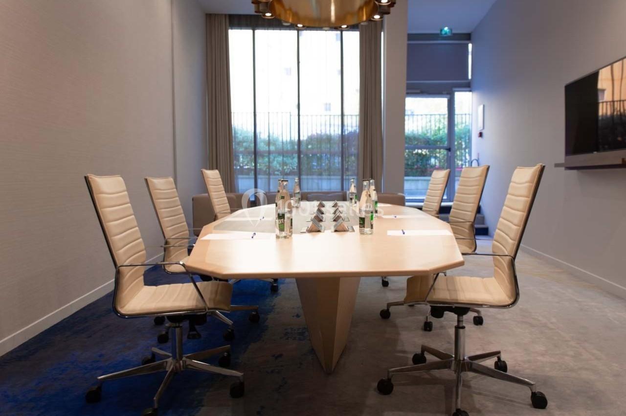 Salle de réunion moderne avec table ovale, chaises en cuir beige, bouteilles d'eau et lumière naturelle.
