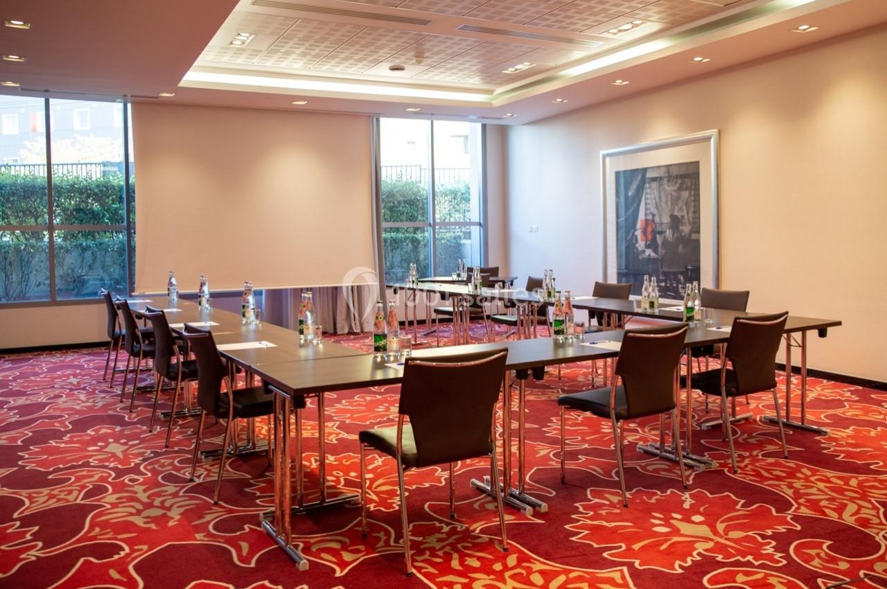 Salle de réunion lumineuse avec tables disposées en U, chaises en cuir, bouteilles d'eau et grandes fenêtres donnant sur l…
