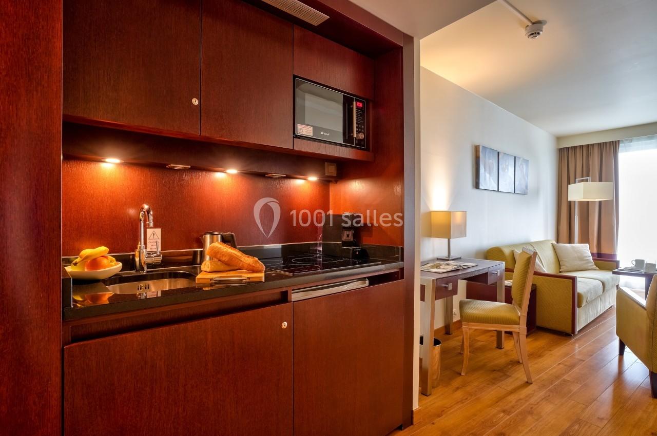 Cuisine intégrée avec micro-ondes, évier, plaques de cuisson et fruits sur le plan de travail, ouverte sur un salon lumineux.