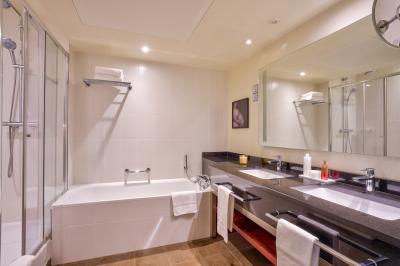 Salle de bain moderne avec baignoire, douche, double vasque, miroir large et serviettes blanches.