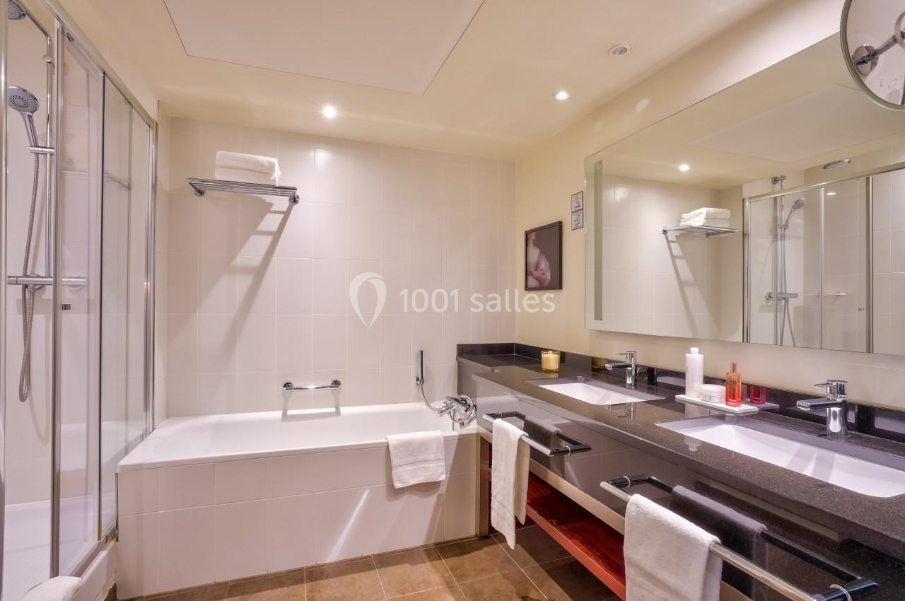 Salle de bain moderne avec baignoire, douche, double vasque, miroir large et serviettes blanches.