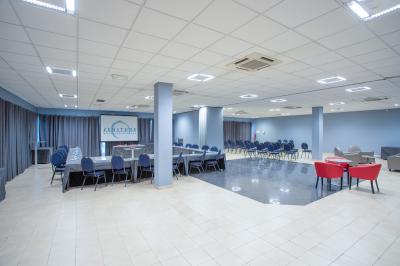 Salle de réunion avec tables disposées en U, chaises bleues et rouges, éclairage au plafond et sol carrelé beige.