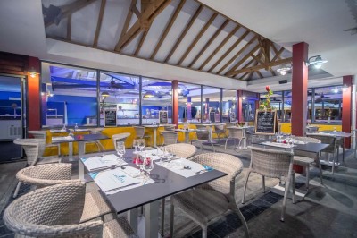 Salle de réunion avec tables disposées en U, chaises bleues et rouges, éclairage au plafond et sol carrelé beige.