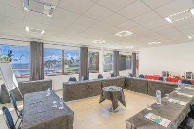 Chambre lumineuse avec lit double, mobilier en bois, télévision et balcon offrant une vue sur des palmiers.