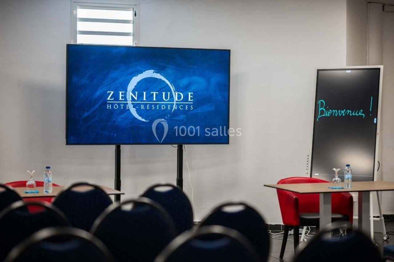 Salle de réunion avec écran affichant ’Zenitude Hôtel-Résidences’, tableau noir ’Bienvenue !’ et chaises disposées.